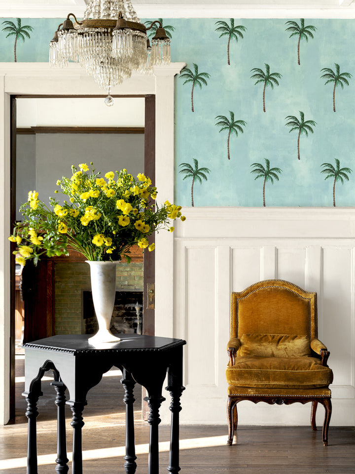 Palm wallpaper wall with green trees pattern on light blue, seen in living room