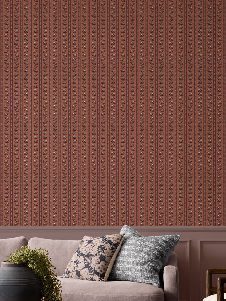 Terracotta lotus stripe wallpaper with a greige sofa and a black urn holding a trailing plant