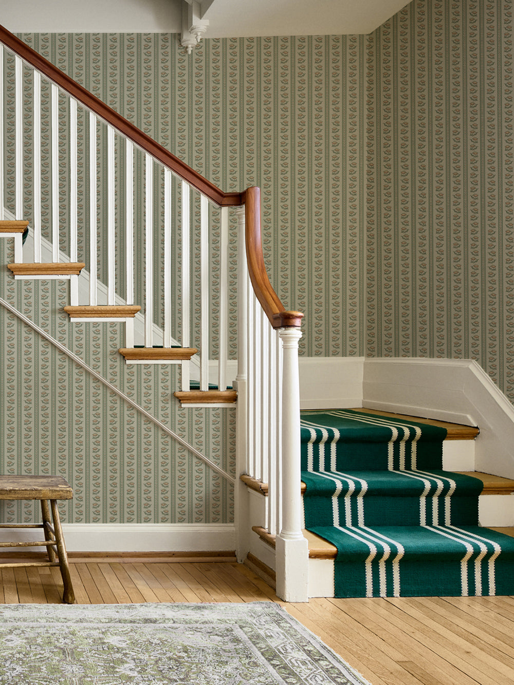 Sage lotus stripe wallpaper in a stairwell with white spindles and a green striped runner