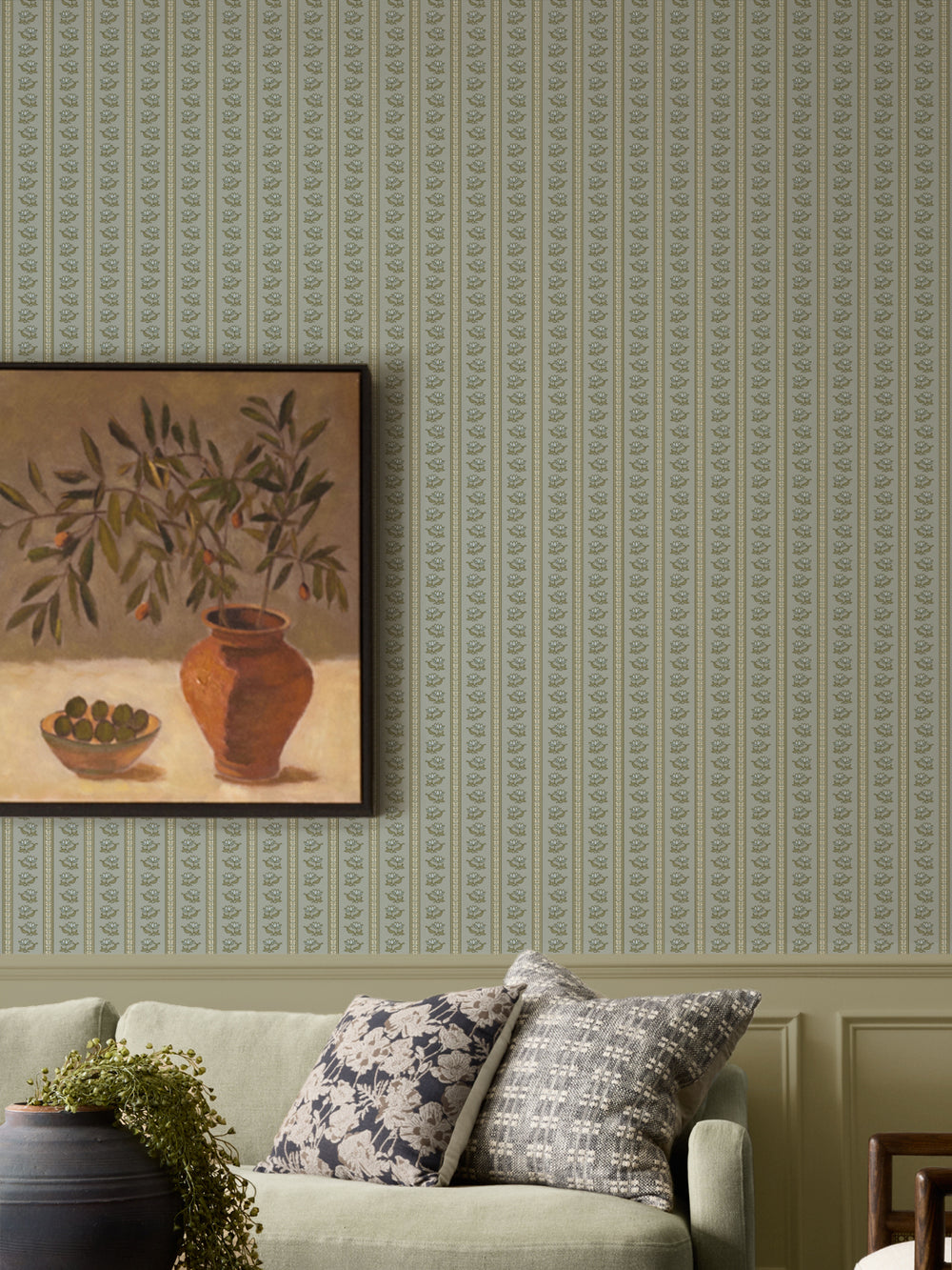 Grey-green lotus stripe wallpaper with a sage sofa and a framed olive-branch still life