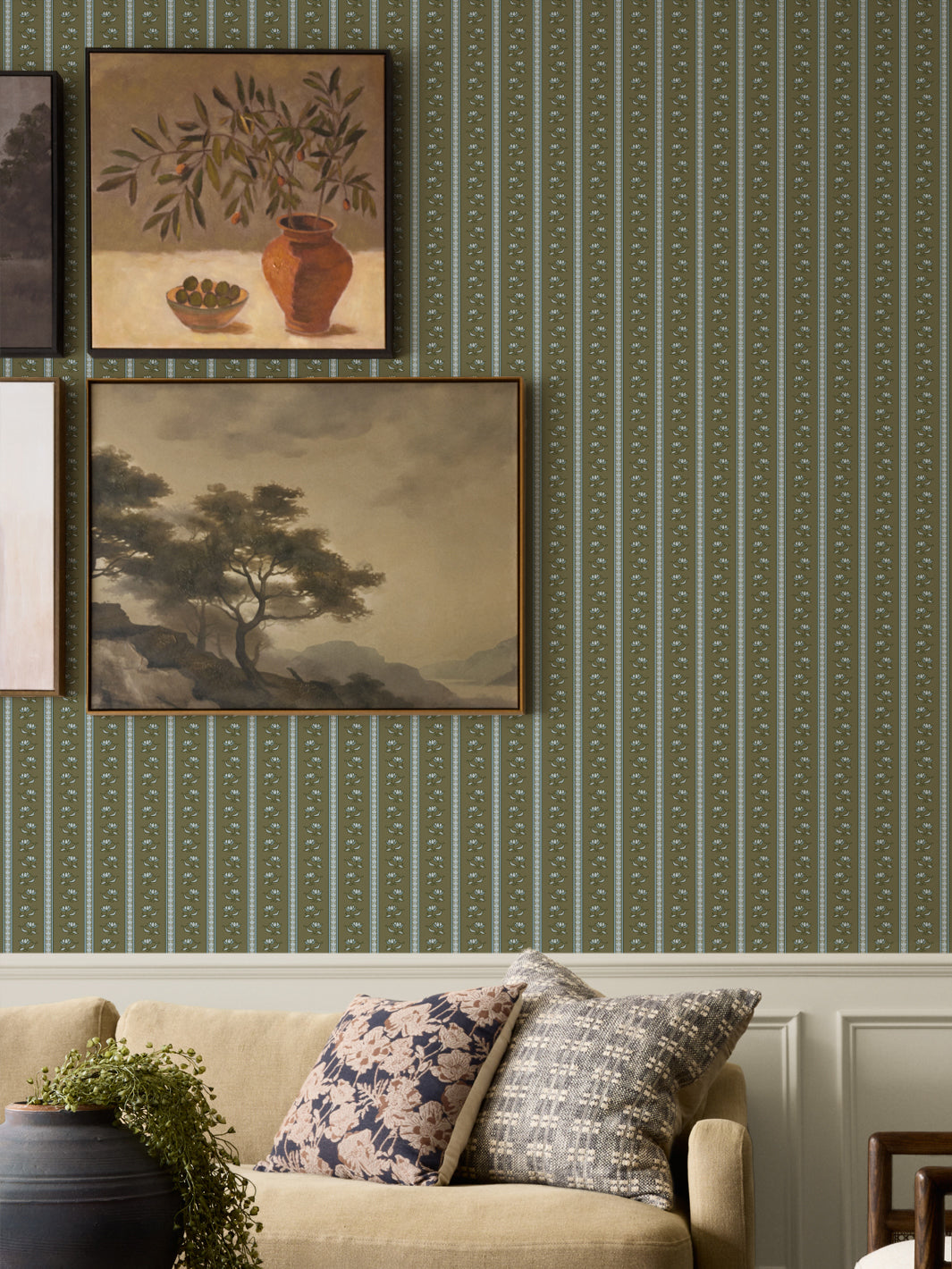 Moss lotus stripe wallpaper on a gallery wall with two framed paintings and an oatmeal sofa