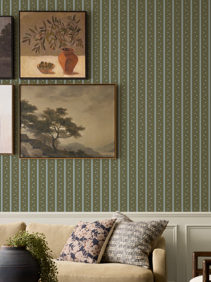 Moss lotus stripe wallpaper on a gallery wall with two framed paintings and an oatmeal sofa