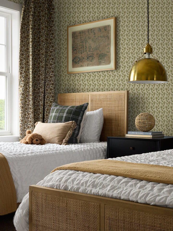 Cane bed with a green plaid cushion and mustard throw, black nightstand and brass pendant