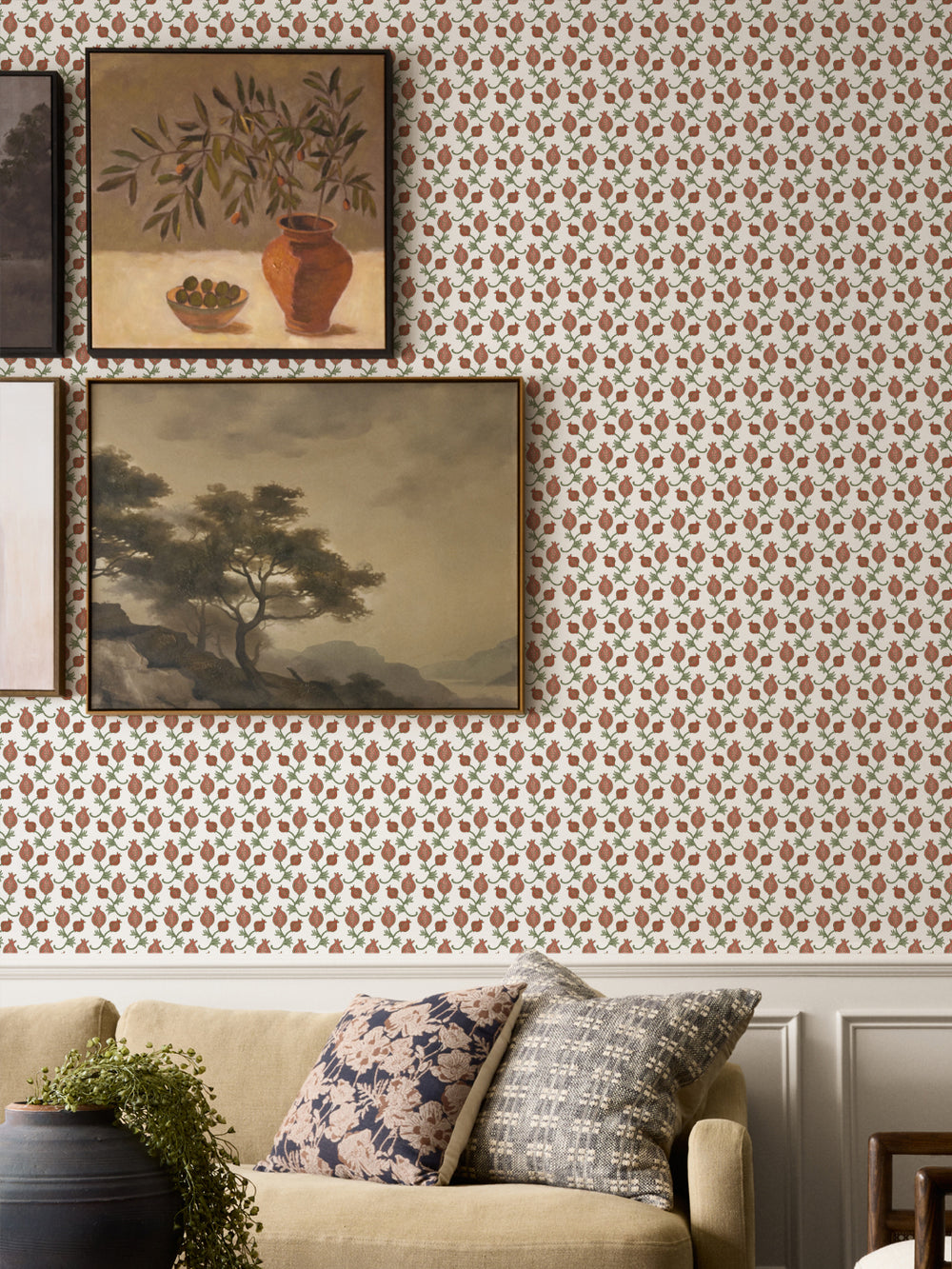 Framed still life and landscape above a tan sofa with floral cushions and a black clay pot