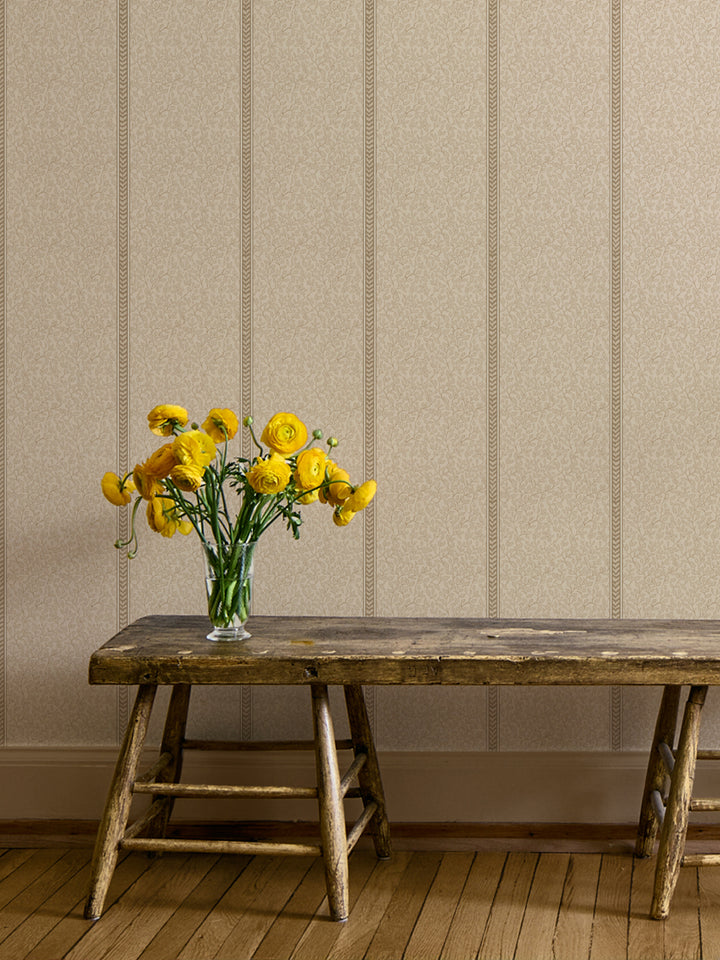 Rustic wood bench with a glass vase of yellow ranunculus against cream vine wallpaper