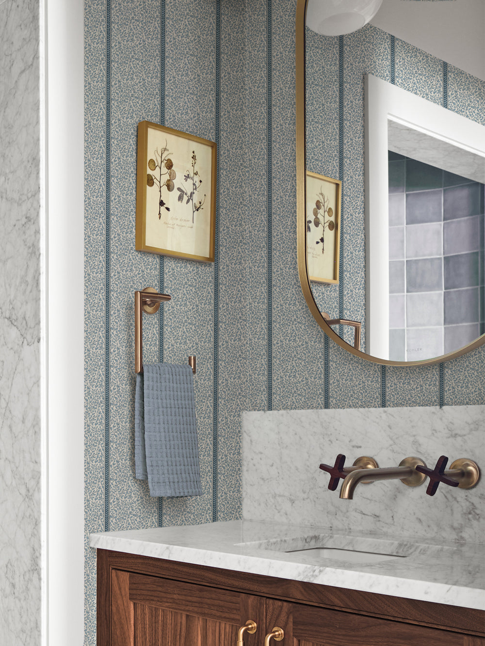 Powder room papered in blue vine wallpaper with marble vanity, brass faucet and botanical print