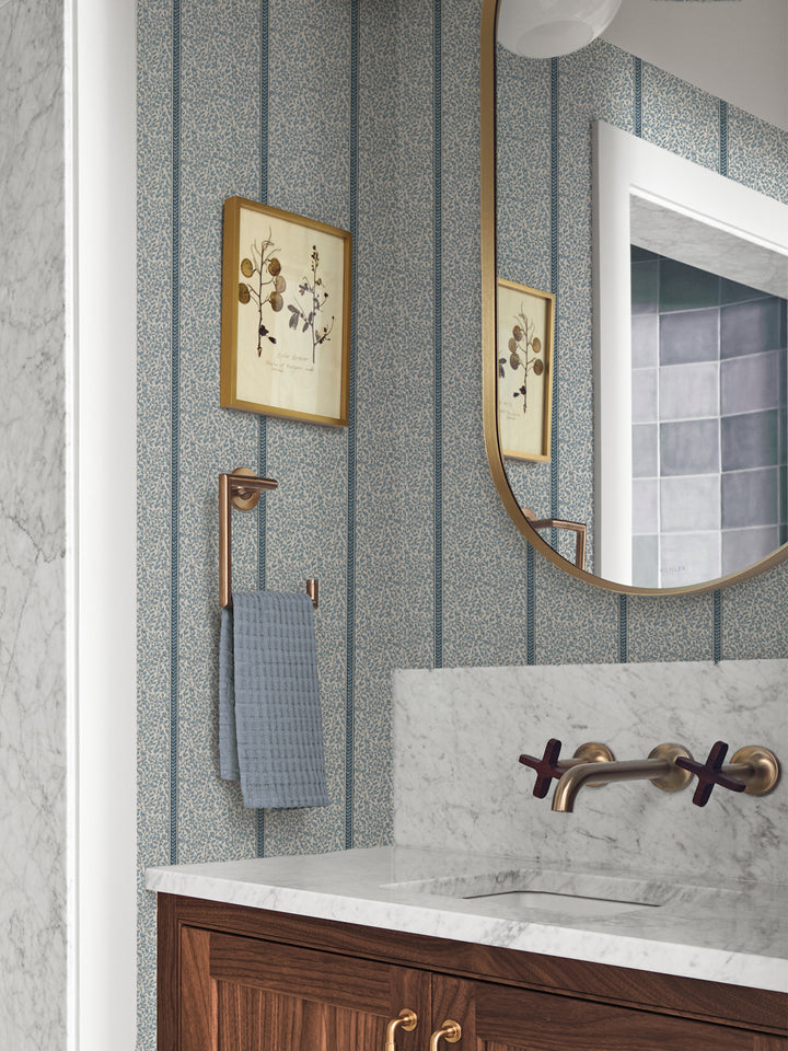 Powder room papered in blue vine wallpaper with marble vanity, brass faucet and botanical print
