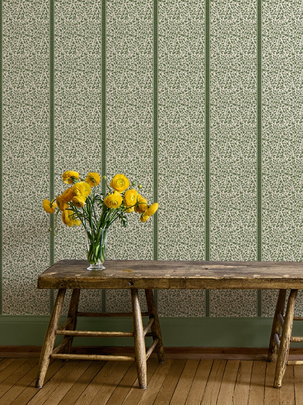 Green Eden vine wallpaper on a hallway wall above a rustic wood bench with yellow ranunculus