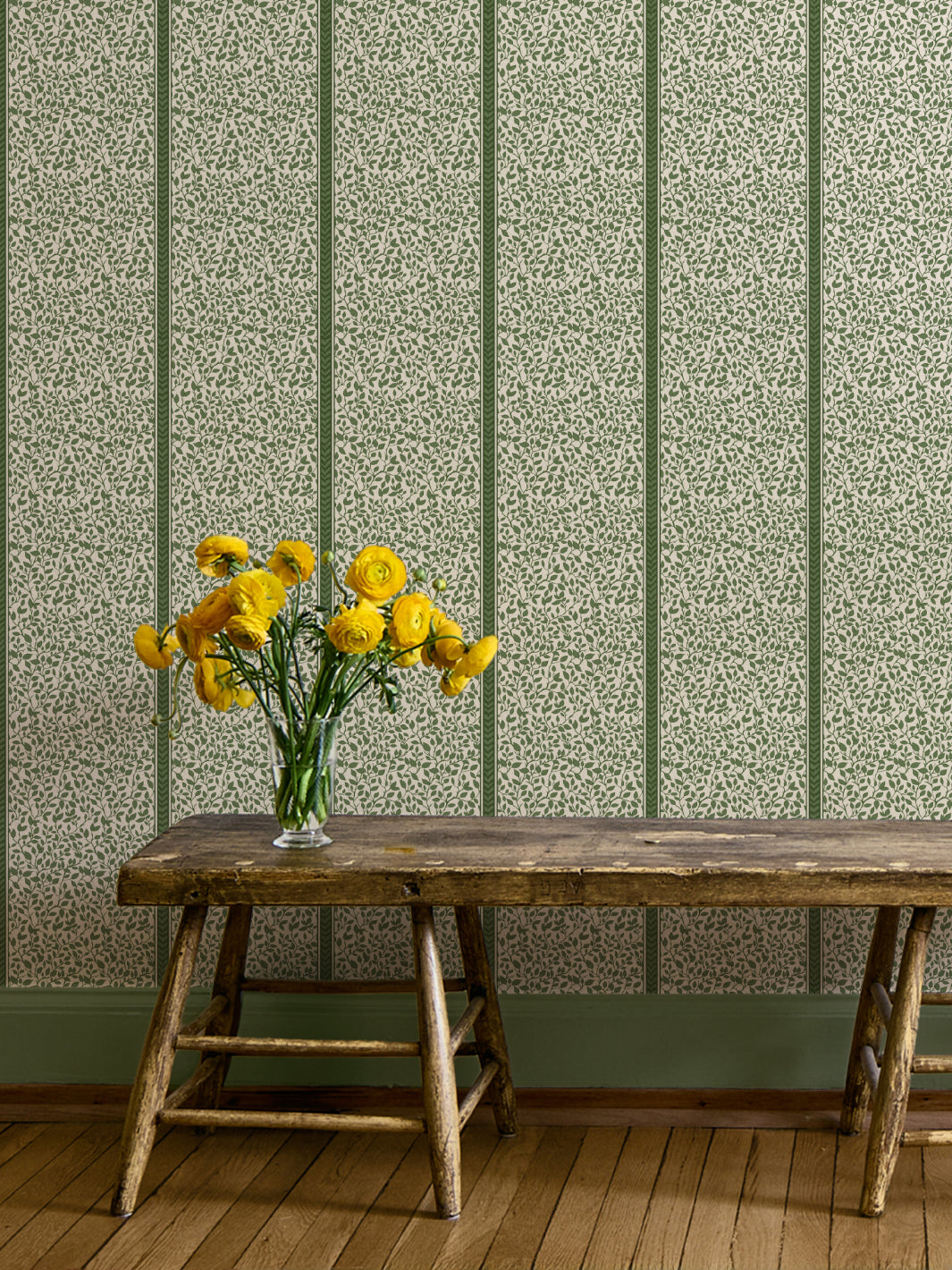 Green Eden vine wallpaper on a hallway wall above a rustic wood bench with yellow ranunculus