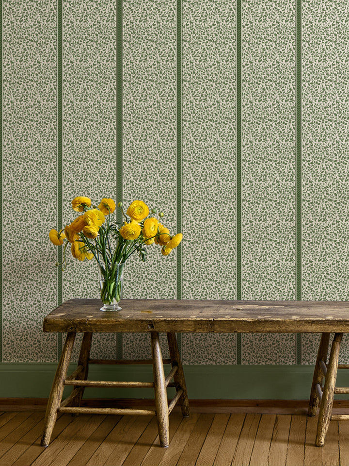 Green Eden vine wallpaper on a hallway wall above a rustic wood bench with yellow ranunculus