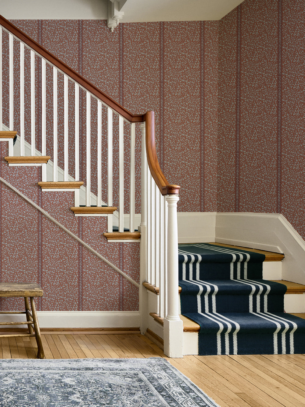 Staircase with white balusters, navy striped runner and a wood bench against terracotta wallpaper