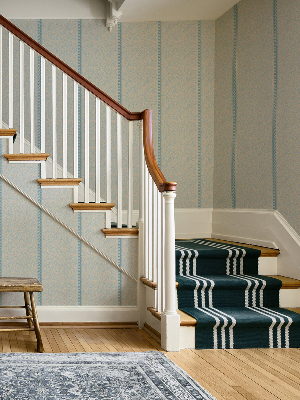 Staircase with white balusters, wood handrail and teal striped runner against blue vine wallpaper