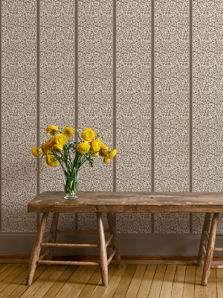 Taupe vine wallpaper behind a rustic wood bench holding a glass vase of yellow ranunculus