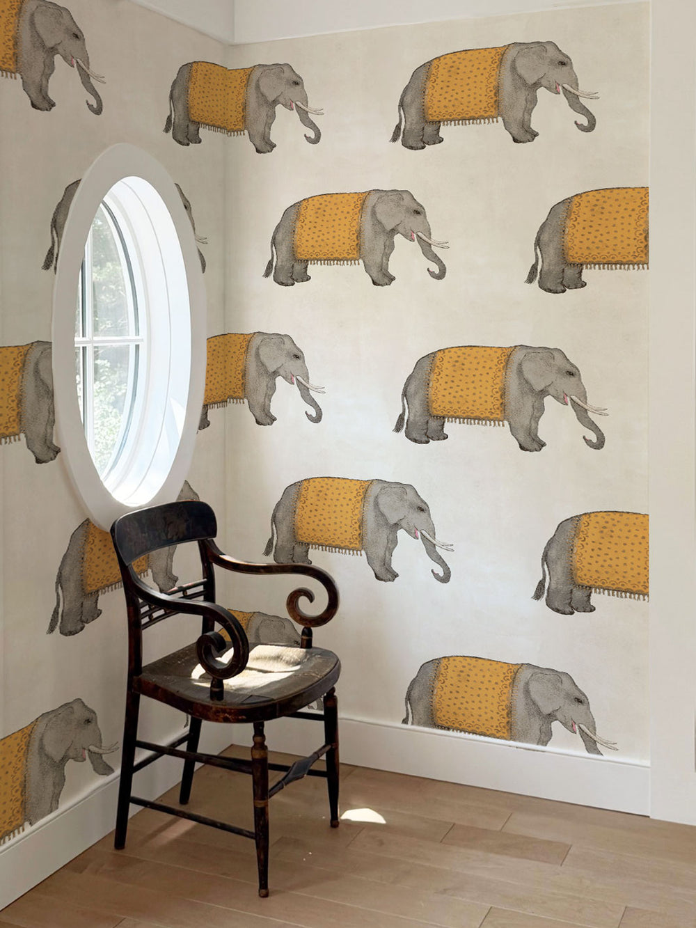 Elephant wallpaper on wall with gray elephants and orange blankets; chair and window visible