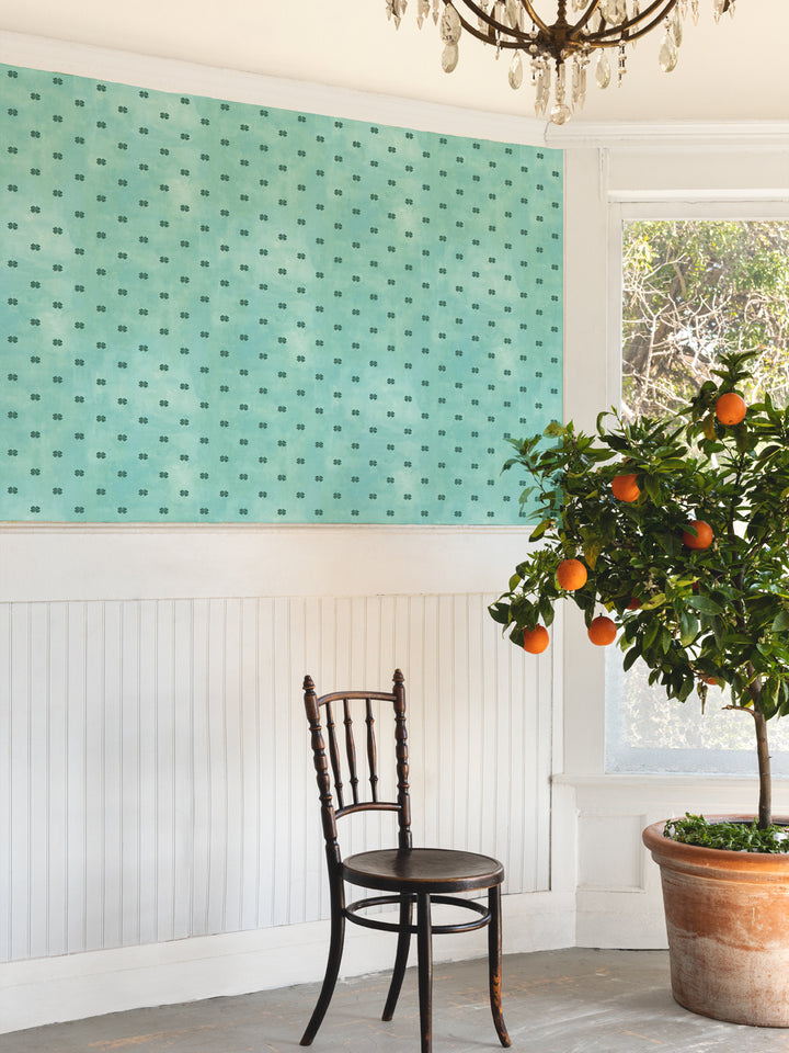 Aqua blue four-leaf clover wallpaper on wall above white wainscot