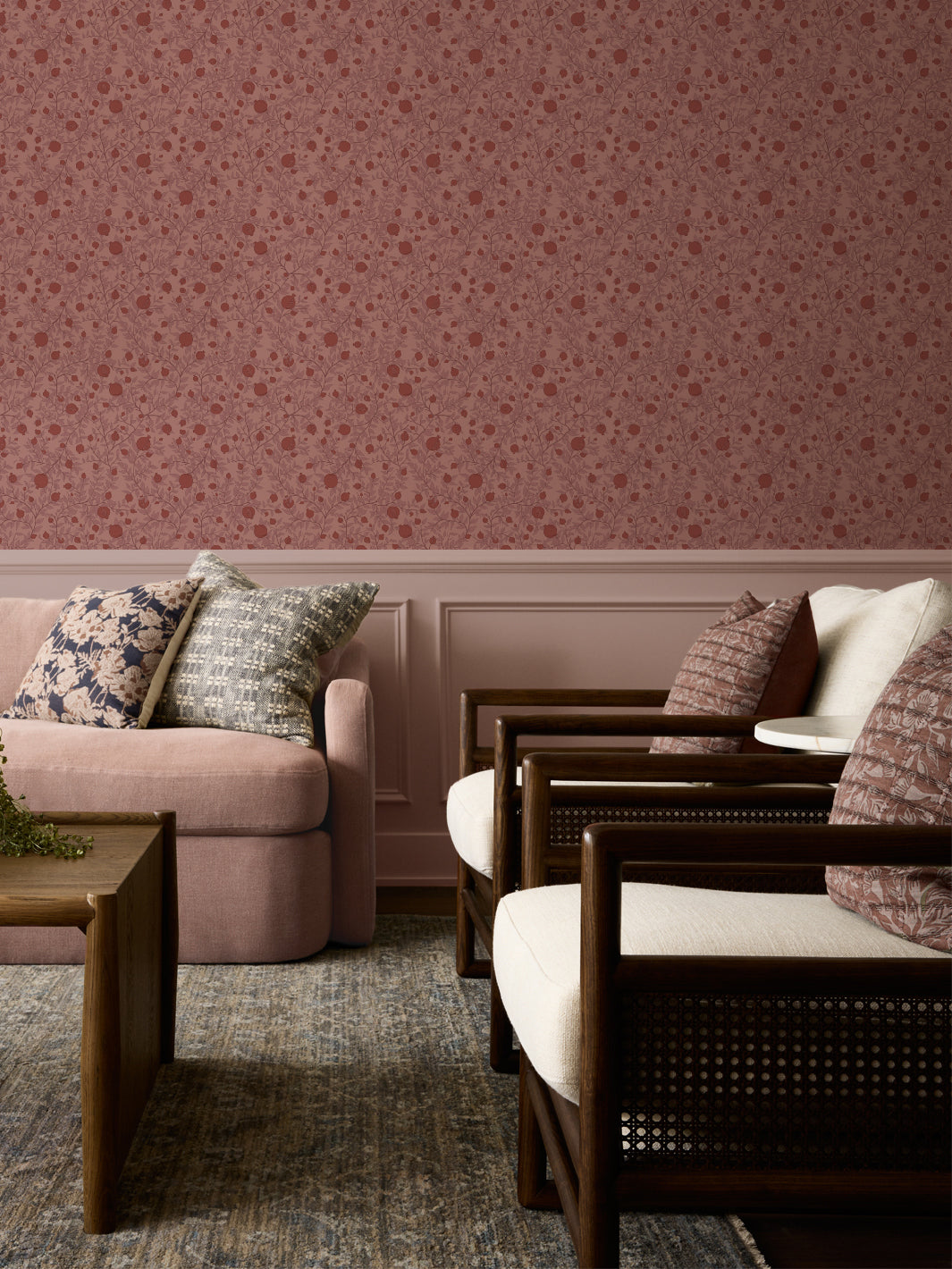 Blush sofa with patterned cushions and cane armchairs below dusty pink pomegranate wallpaper