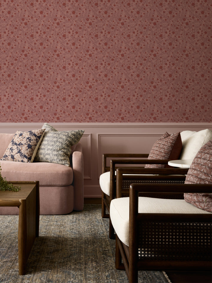 Blush sofa with patterned cushions and cane armchairs below dusty pink pomegranate wallpaper