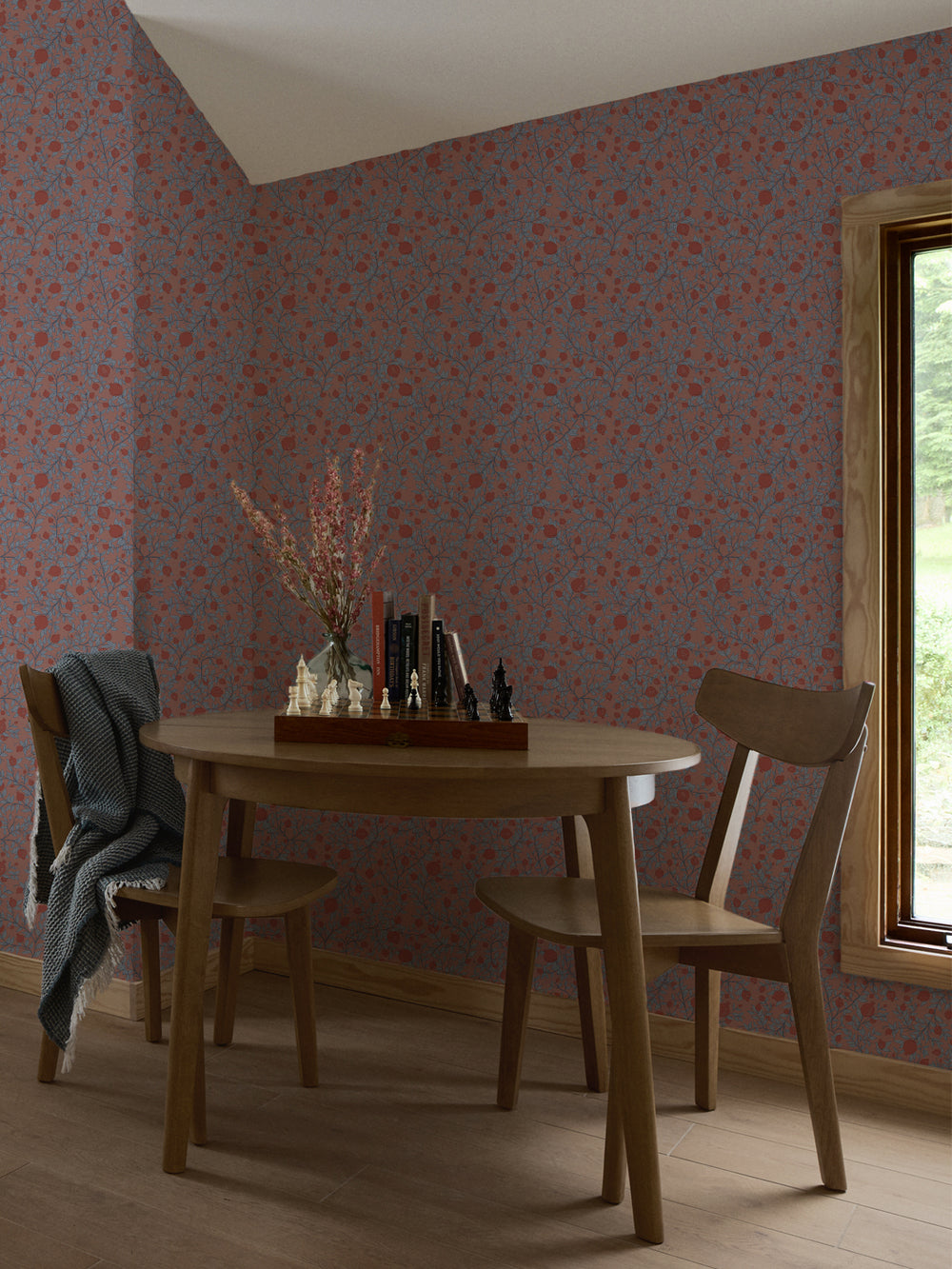 Round oak table and two chairs with a chess set and books against clay pink pomegranate wallpaper