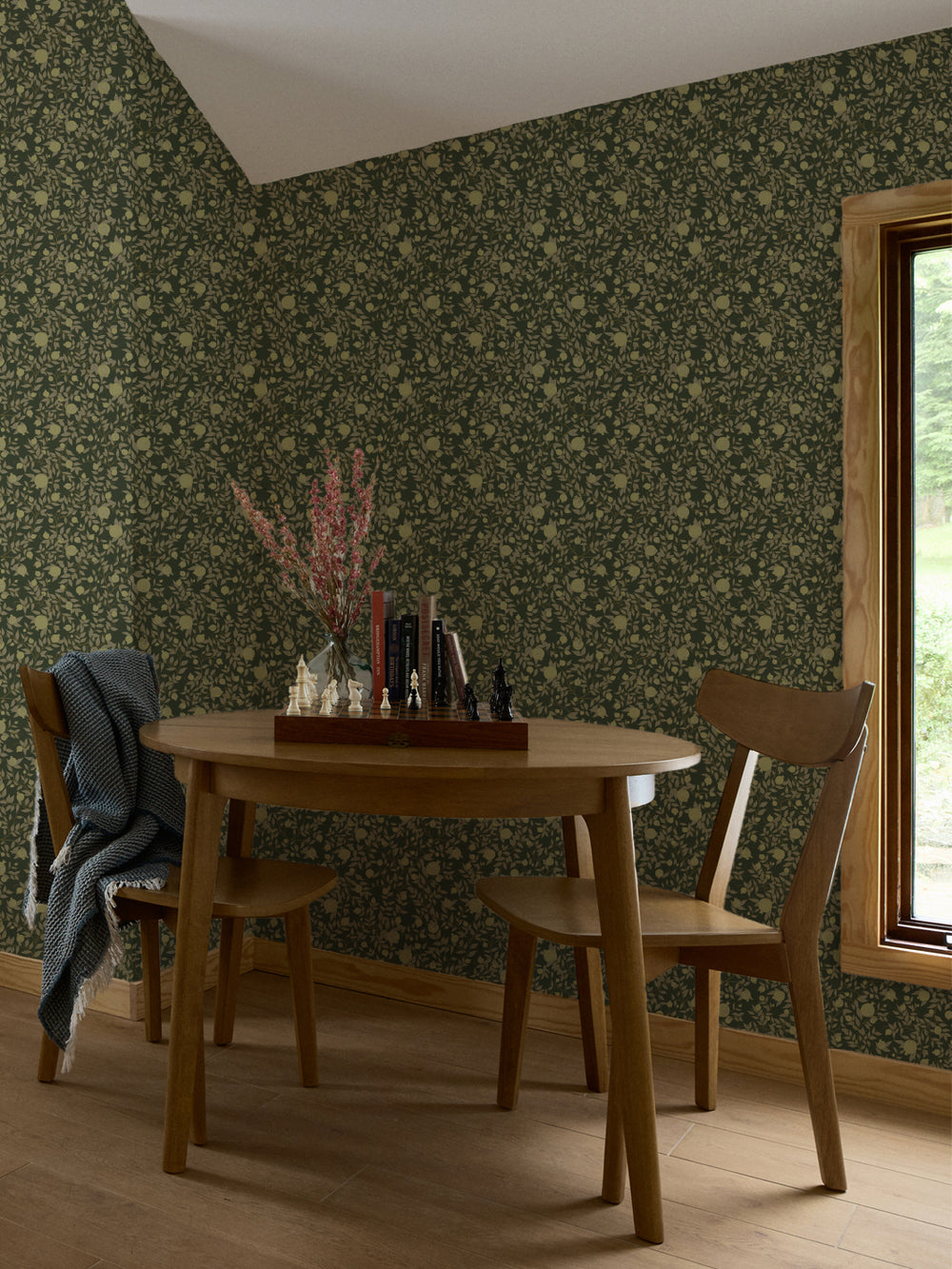Round oak table and two chairs with a chess set against dark olive pomegranate wallpaper
