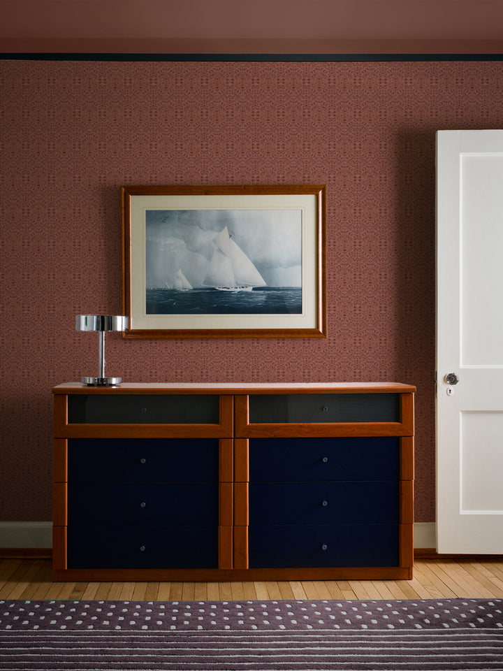 Terracotta Liliana wallpaper behind a cherry dresser with navy drawers and a framed sailboat print