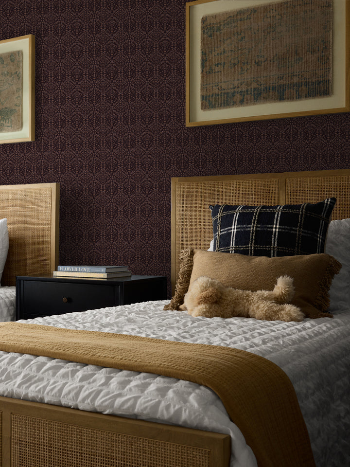 Dark plum Liliana wallpaper in a bedroom with cane headboards and framed antique textiles