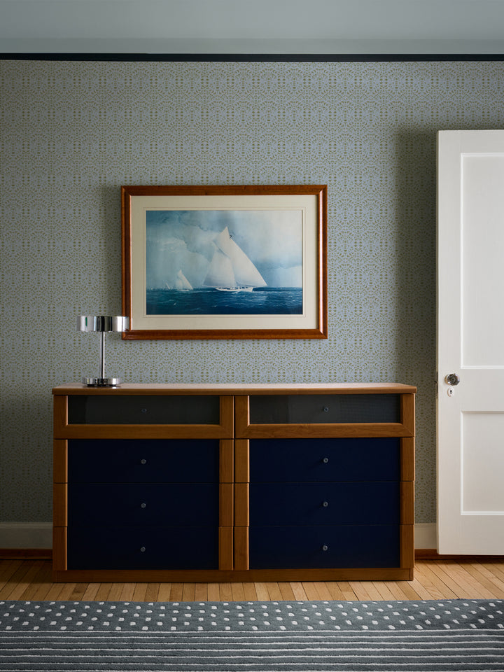 Pale blue Liliana wallpaper behind a cherry dresser with navy drawers and a framed sailboat watercolour