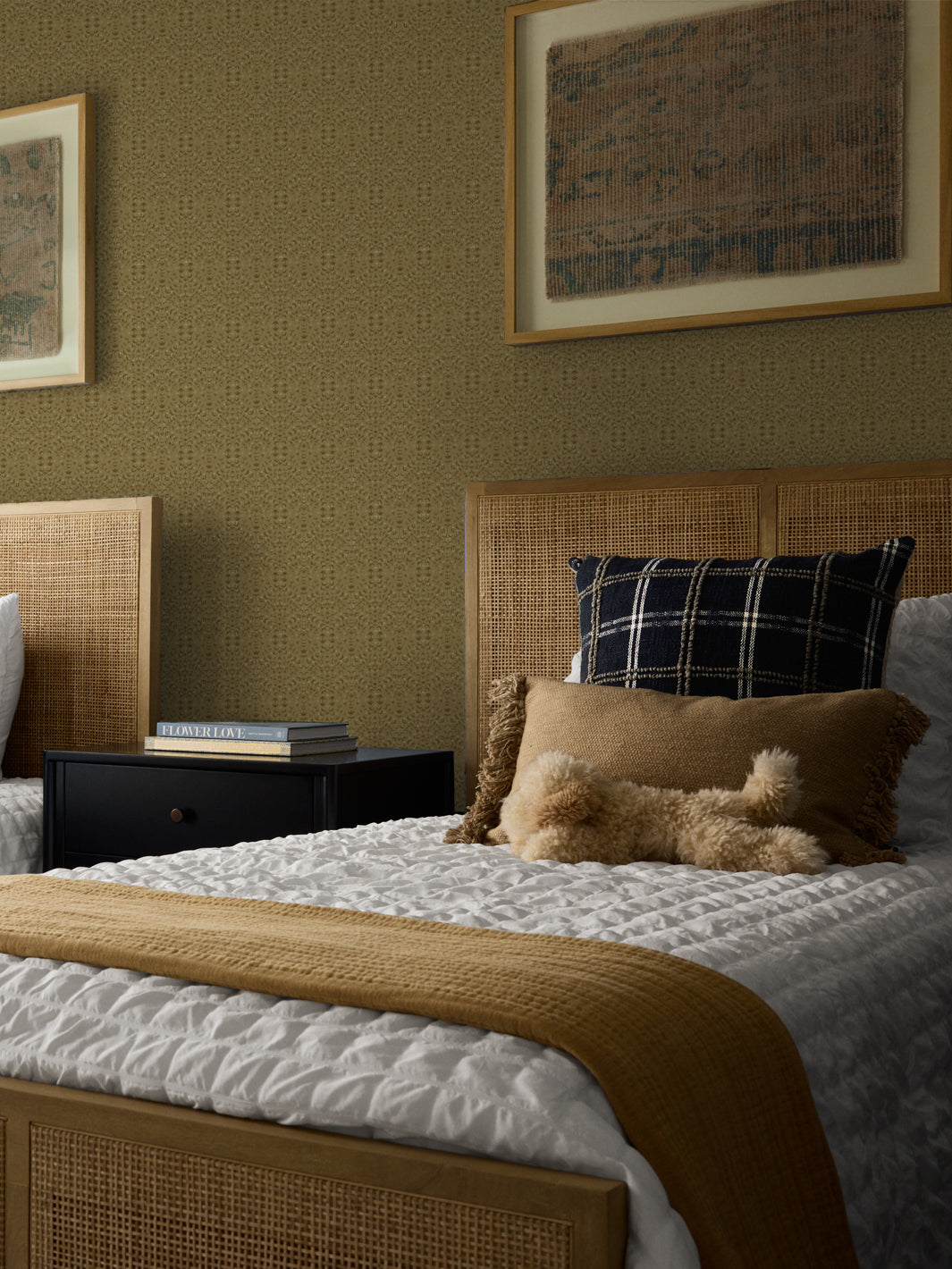 Khaki-gold Liliana wallpaper in a bedroom with cane headboards and framed antique textiles
