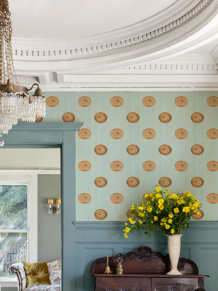 Blue wallpaper with repeating gold oval eye motif on a wall
