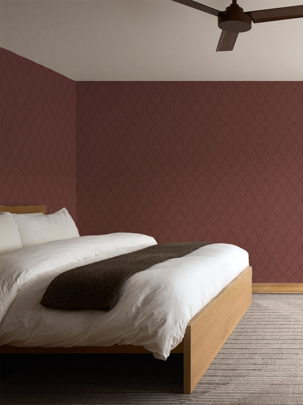 Burgundy leaf-trellis wallpaper in a bedroom with an oak platform bed, white duvet and ceiling fan