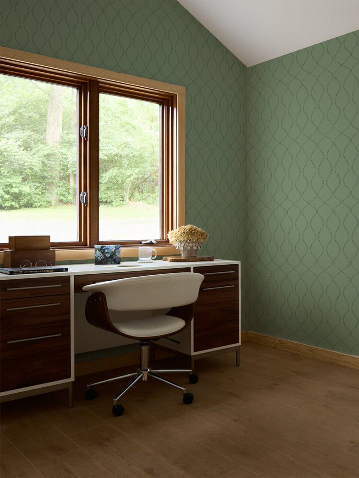 Green trellis wallpaper in a study with a walnut desk, white swivel chair and dried hydrangeas