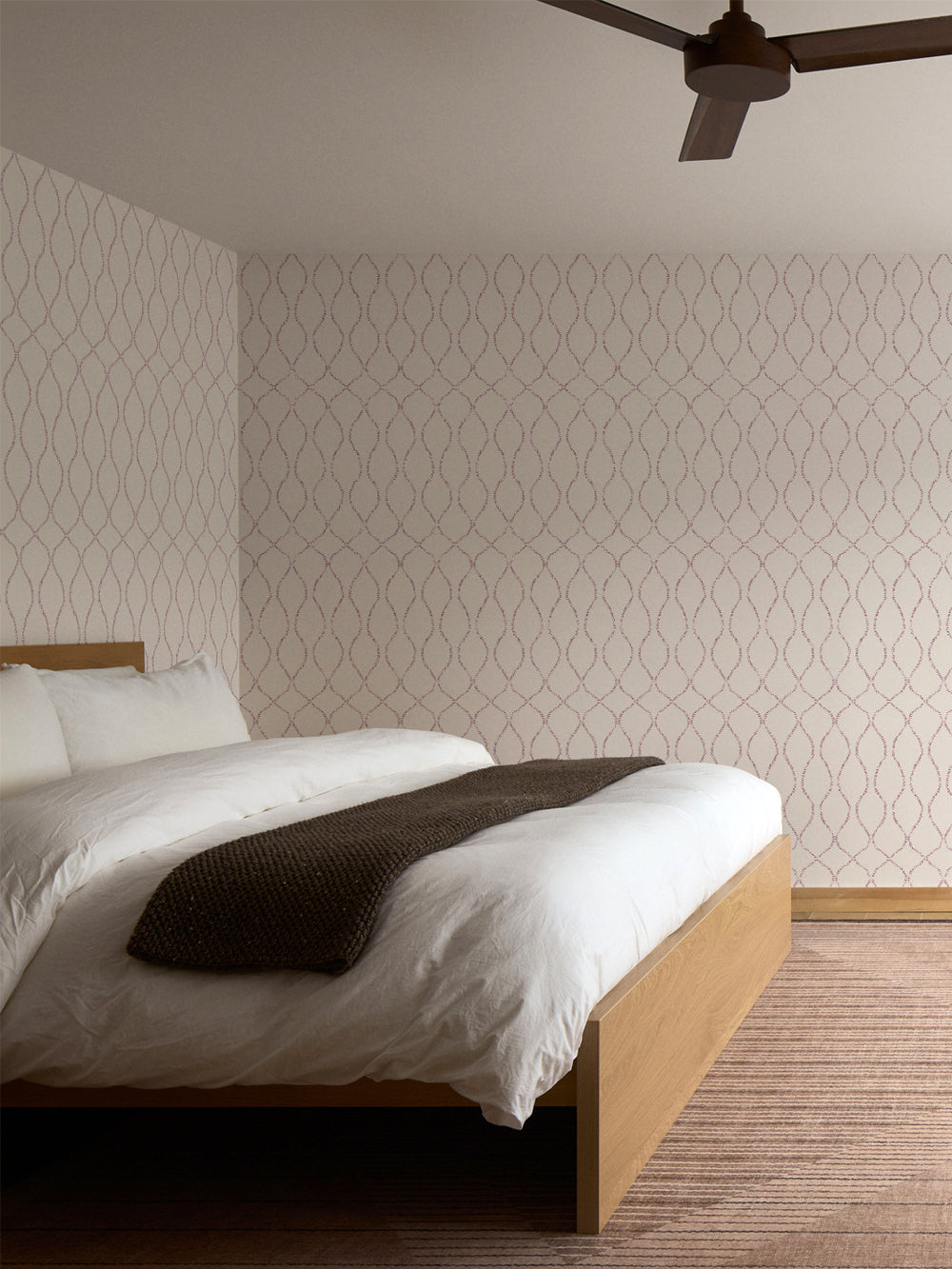 Mauve-on-cream trellis wallpaper behind an oak bed with a white duvet and terracotta rug