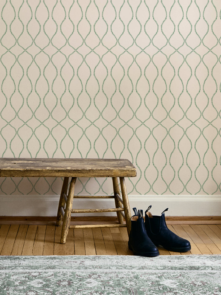 Green-on-cream trellis wallpaper above a rustic wood bench with navy boots and a faded rug