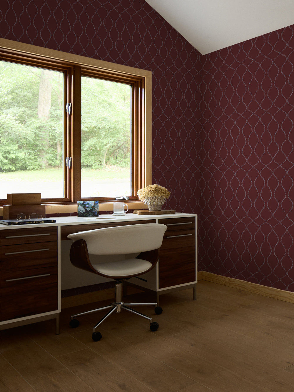 Merlot trellis wallpaper in a study with a walnut desk, white swivel chair and dried hydrangeas