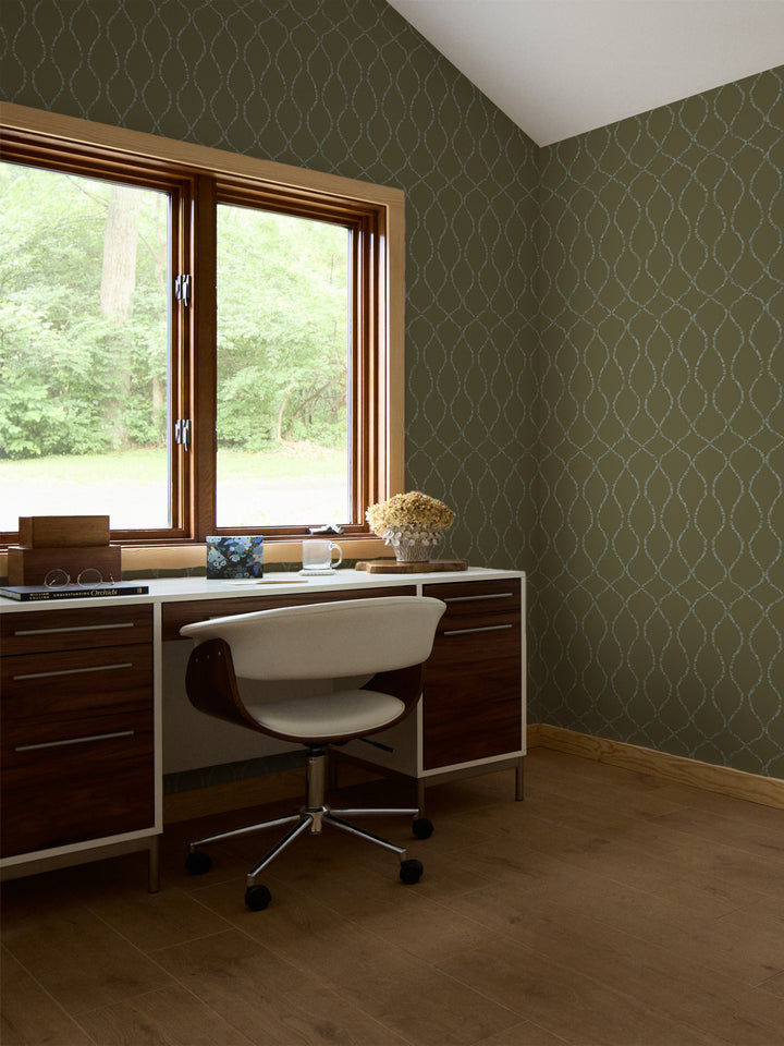 Olive trellis wallpaper in a study with a walnut desk, white swivel chair and stacked books