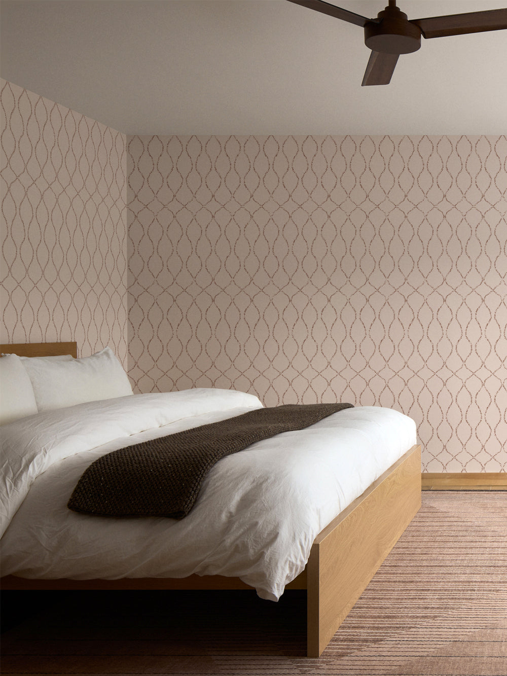 Blush trellis wallpaper behind an oak bed with white bedding and a rust striped rug