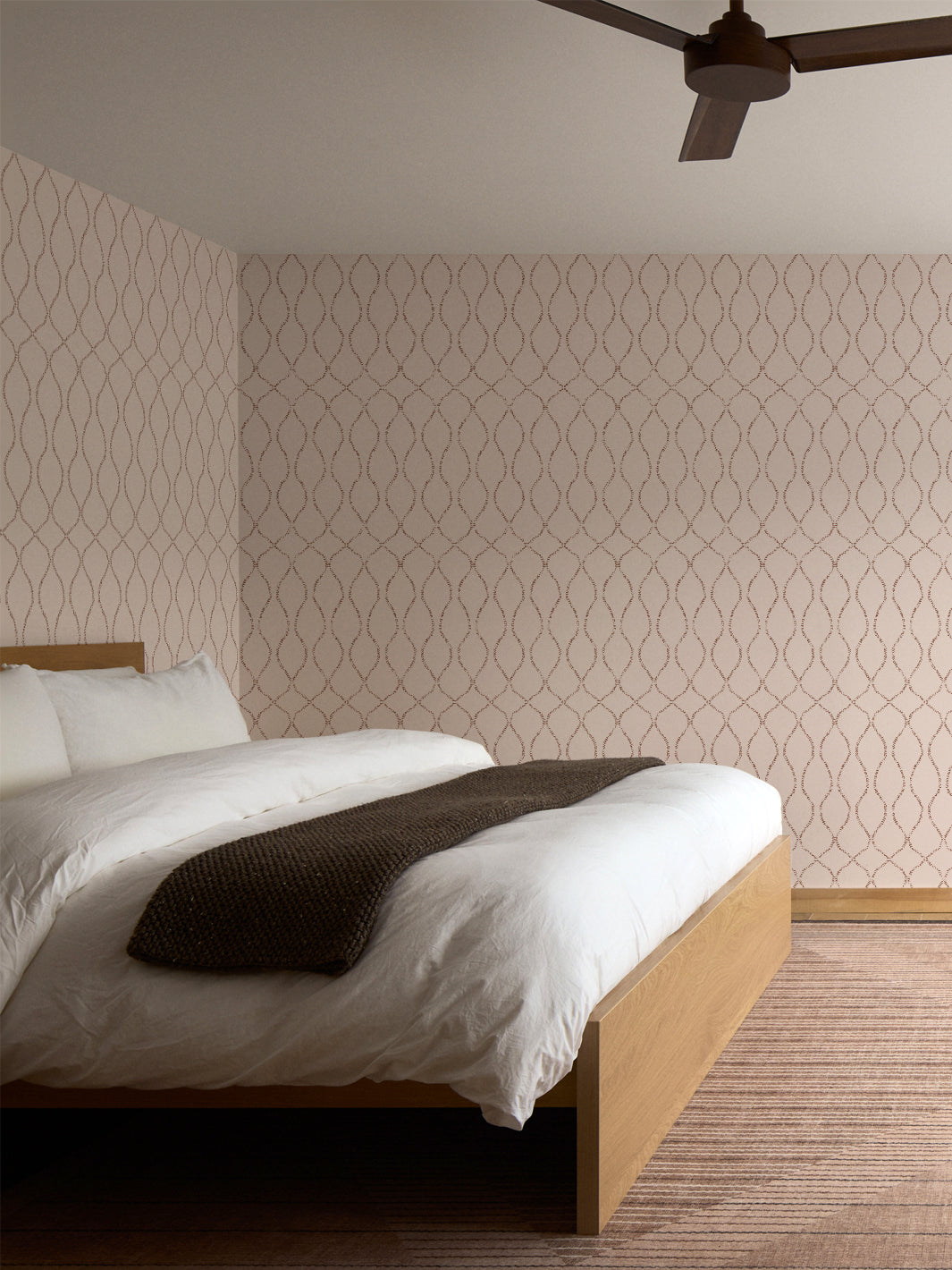 Blush trellis wallpaper behind an oak bed with white bedding and a rust striped rug