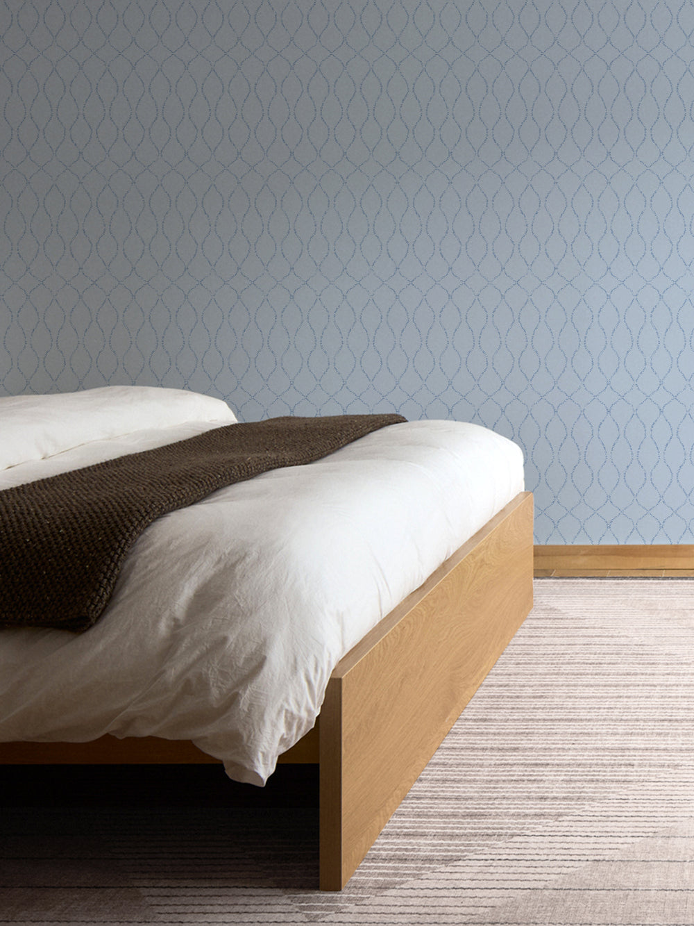 Light blue trellis wallpaper beside an oak bed with a white duvet and pale striped rug