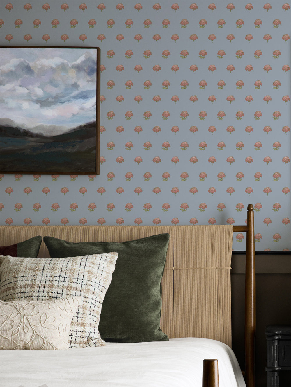 Bedroom wall in pale blue peony wallpaper with a cane headboard and framed landscape painting