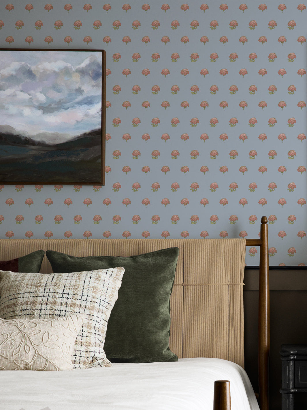 Bedroom wall in pale blue peony wallpaper with a cane headboard and framed landscape painting