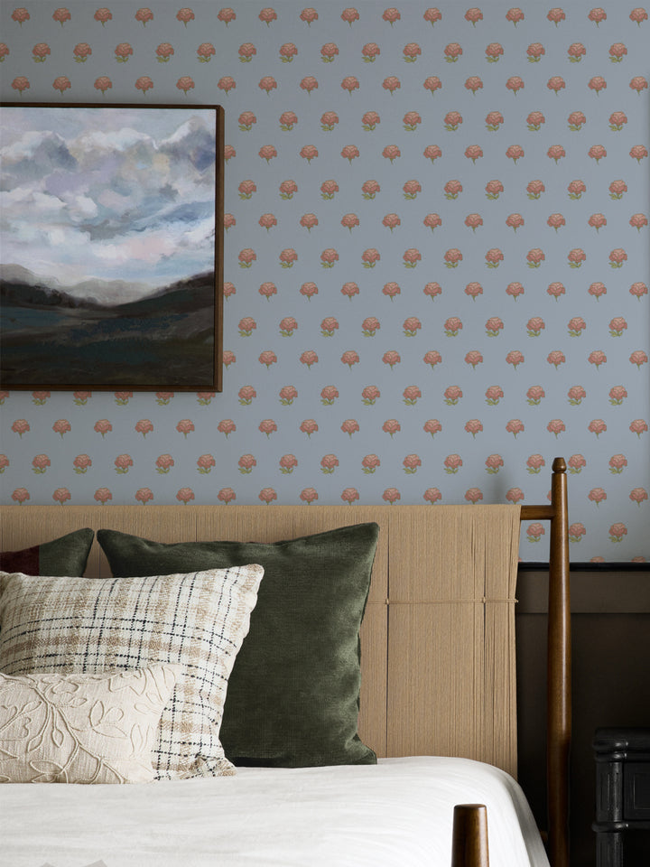 Bedroom wall in pale blue peony wallpaper with a cane headboard and framed landscape painting