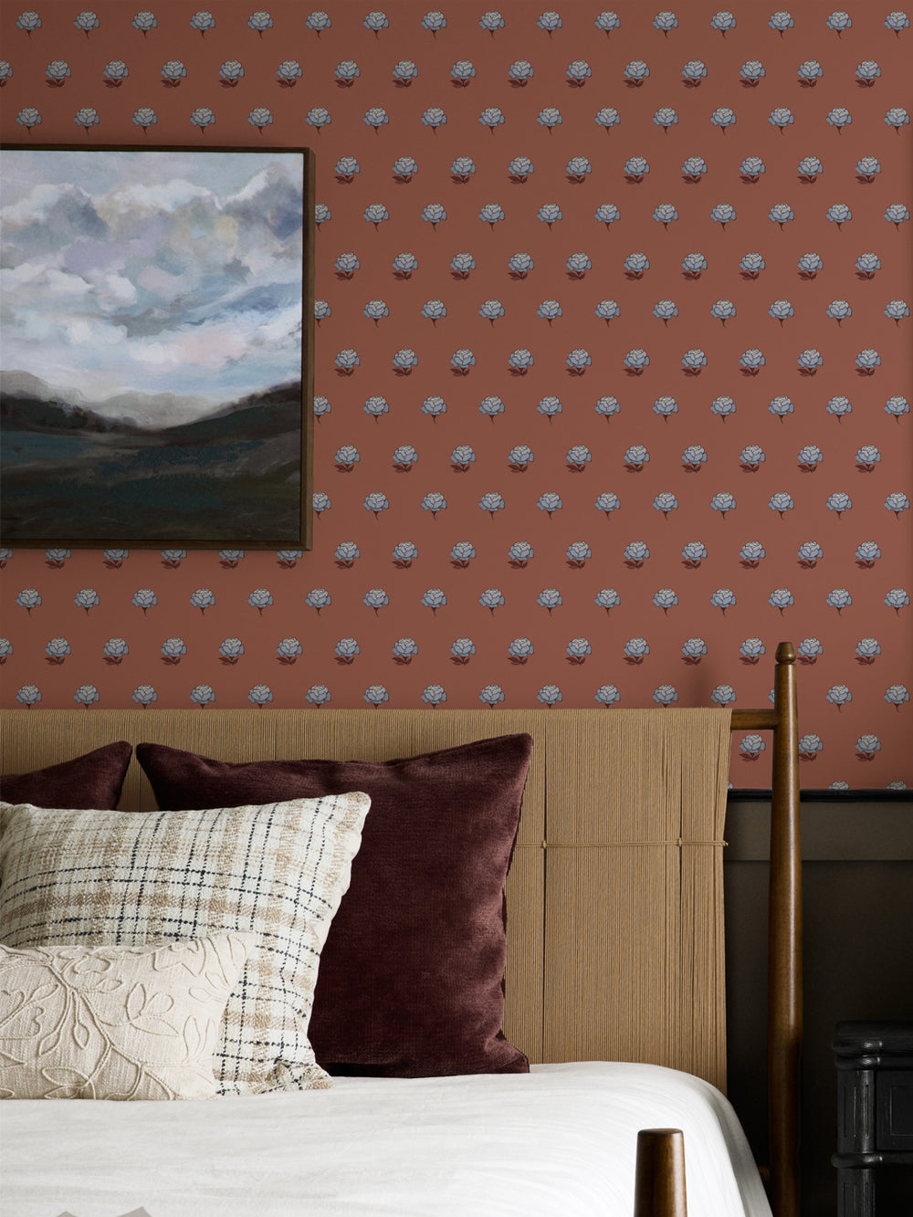 Bedroom wall in blue on terracotta peony wallpaper with a cane headboard and framed landscape