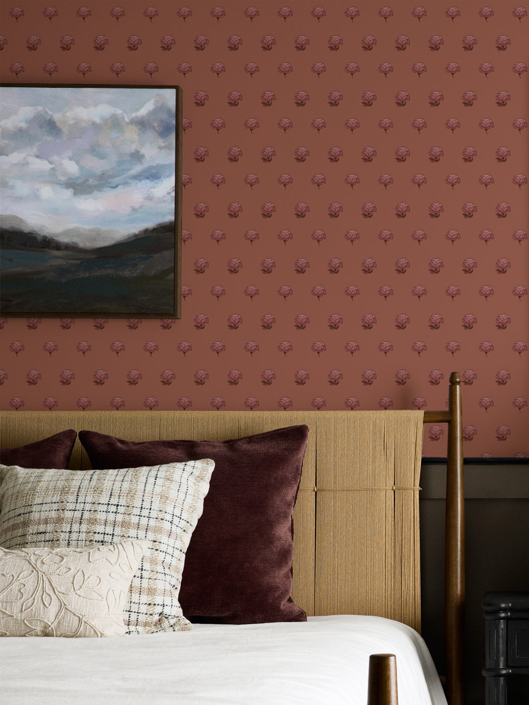 Bedroom wall in tonal rose and clay peony wallpaper with a cane headboard and cloud landscape