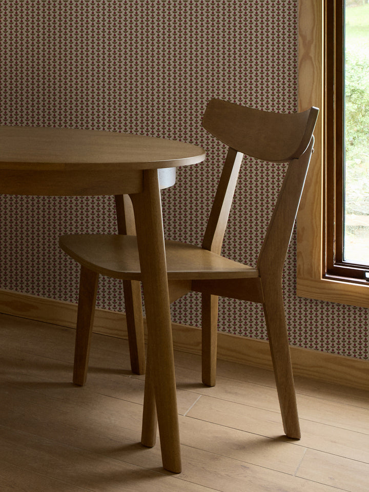Crimson and olive Pomara Bloom wallpaper behind a round oak dining table and chair by a window