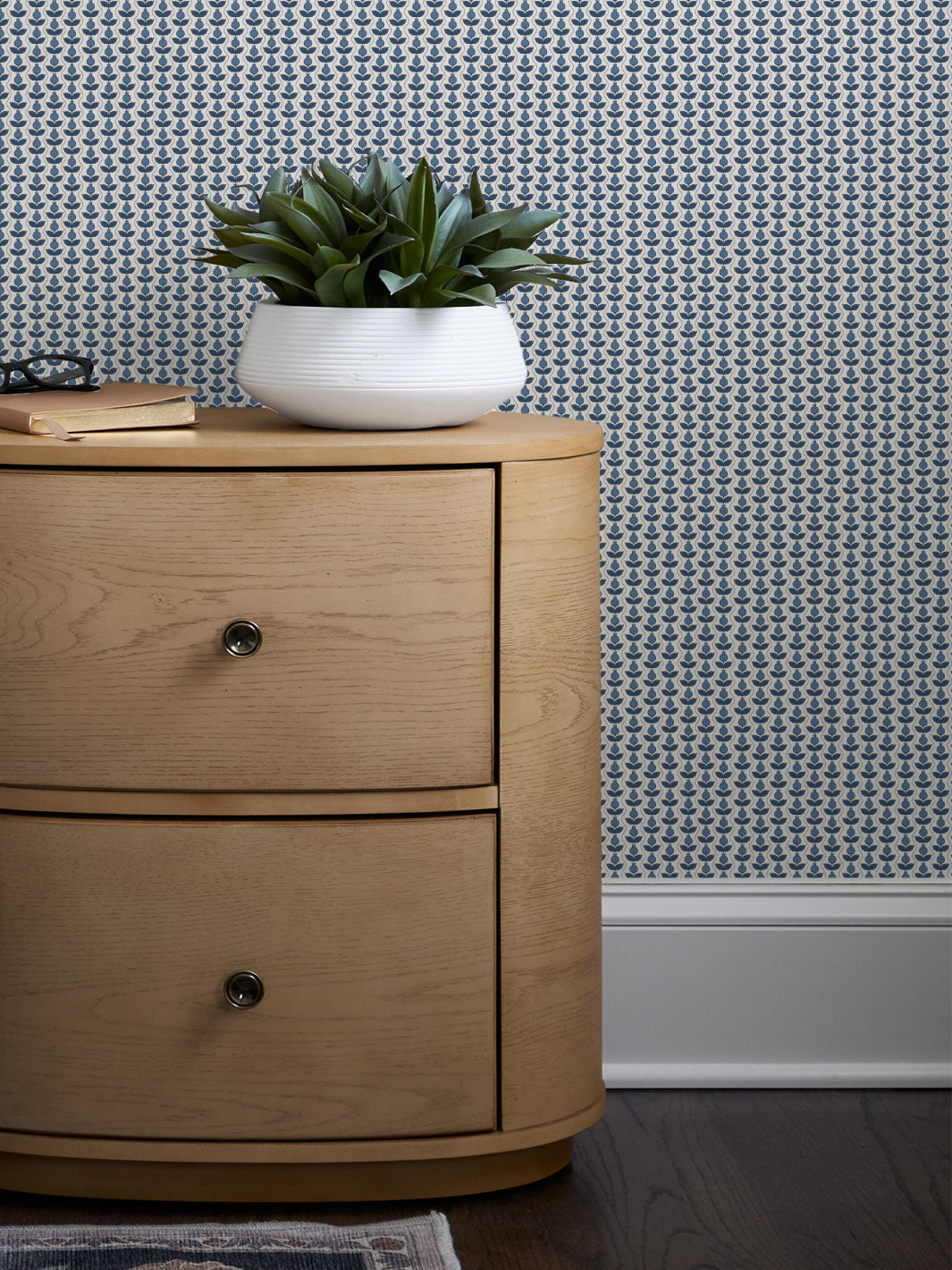 Blue and white Pomara Bloom wallpaper behind a round oak nightstand with a white bowl planter