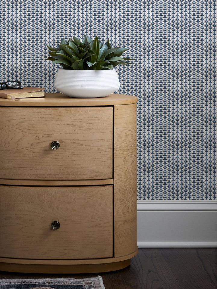 Blue and white Pomara Bloom wallpaper behind a round oak nightstand with a white bowl planter