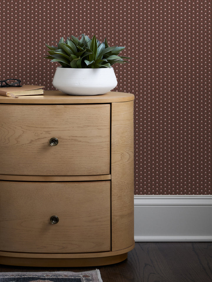 Brown and pink Pomara Bloom wallpaper behind a round oak nightstand with a white bowl planter