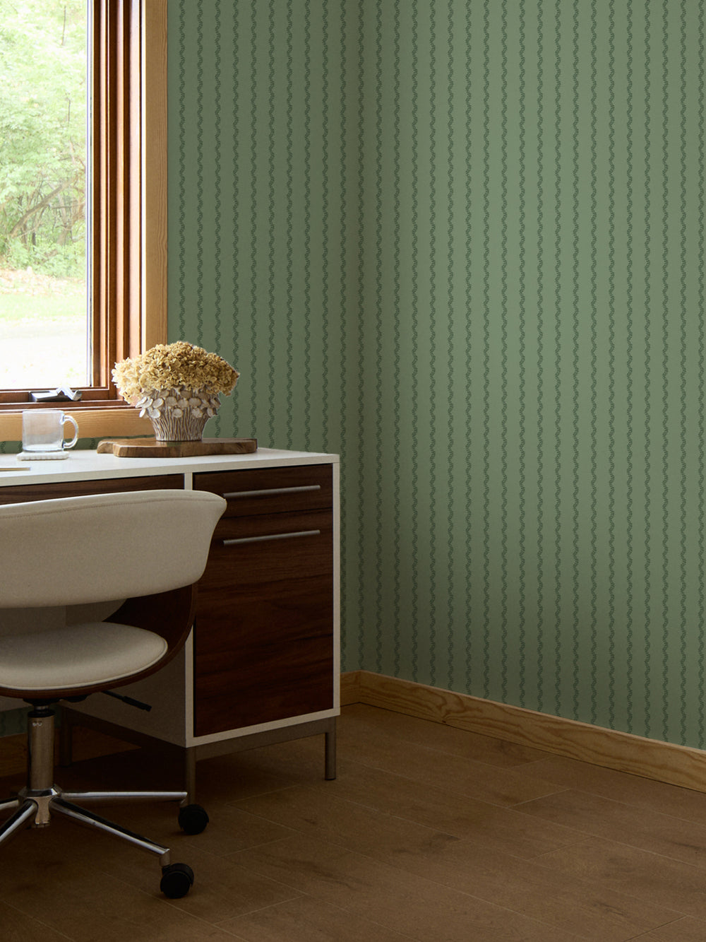 Sage green fern stripe wallpaper behind a walnut desk with a dried hydrangea bouquet