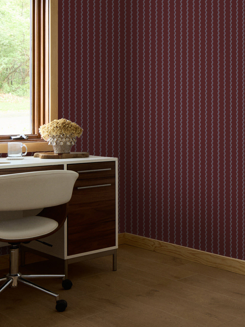 Merlot and blue stripe wallpaper behind a walnut desk with a white swivel chair and hydrangeas