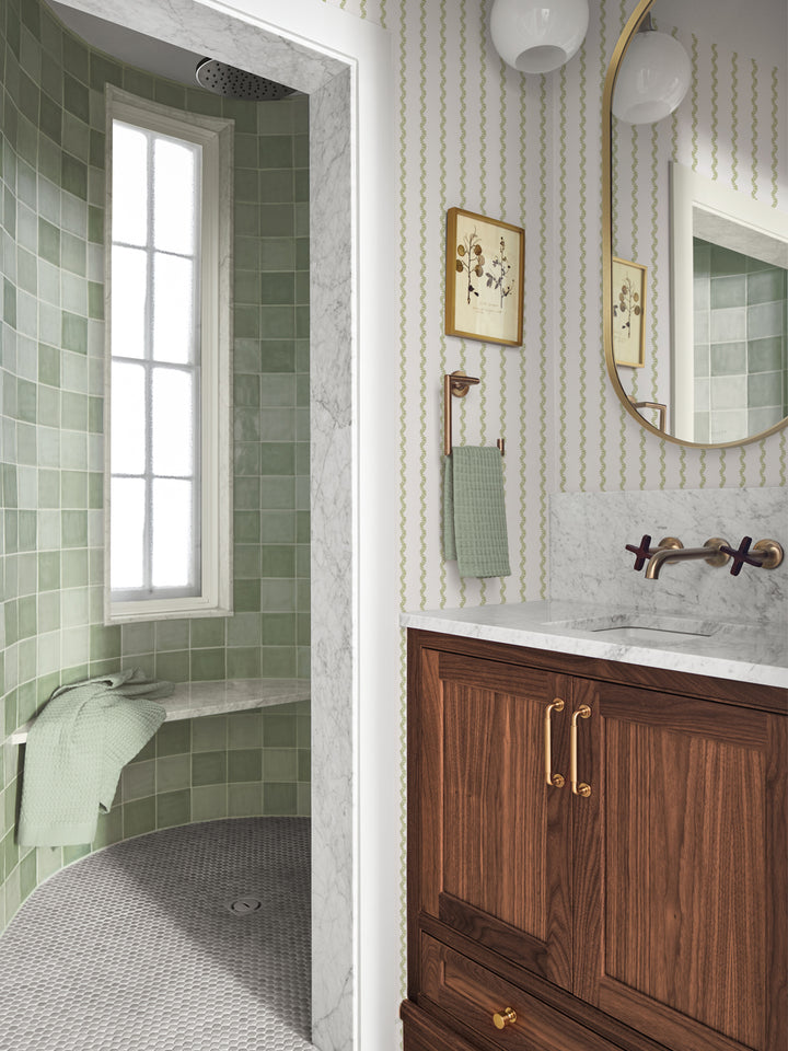 White and green stripe wallpaper in a bath with green tile shower and round brass mirror