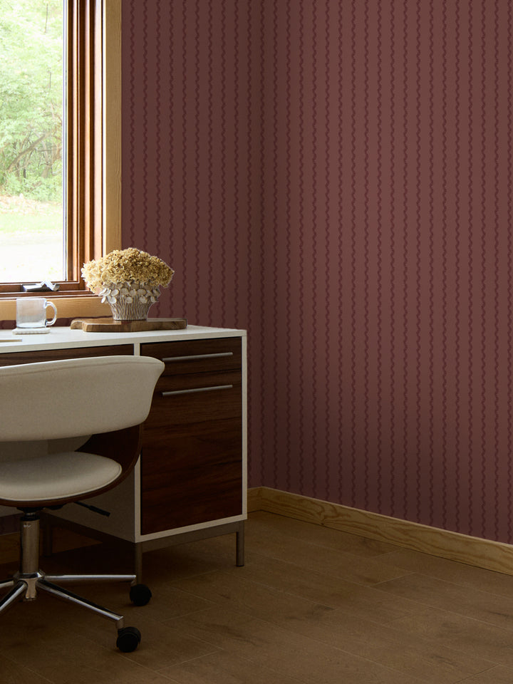 Brick-rose fern stripe wallpaper behind a walnut desk, white swivel chair and dried hydrangeas